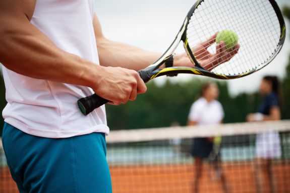 Mann hält einen Tennisball und Schläger